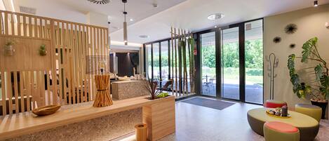 Un área de recepción moderna con un mostrador de madera, zona de estar y ventanas amplias que ofrecen vistas al exterior.