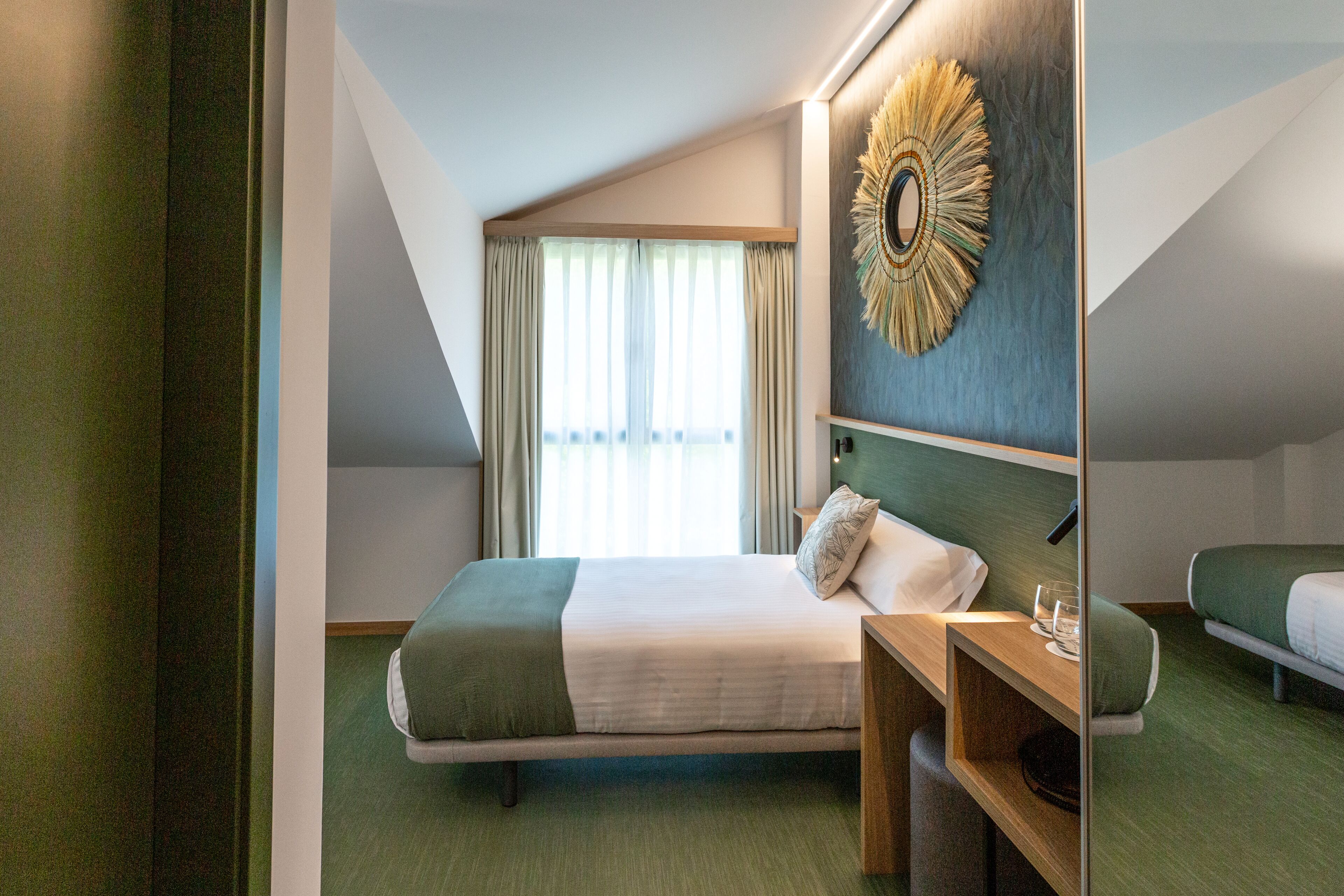 A hotel room with a large bed, a bedside table, a mirror, and a window with curtains.