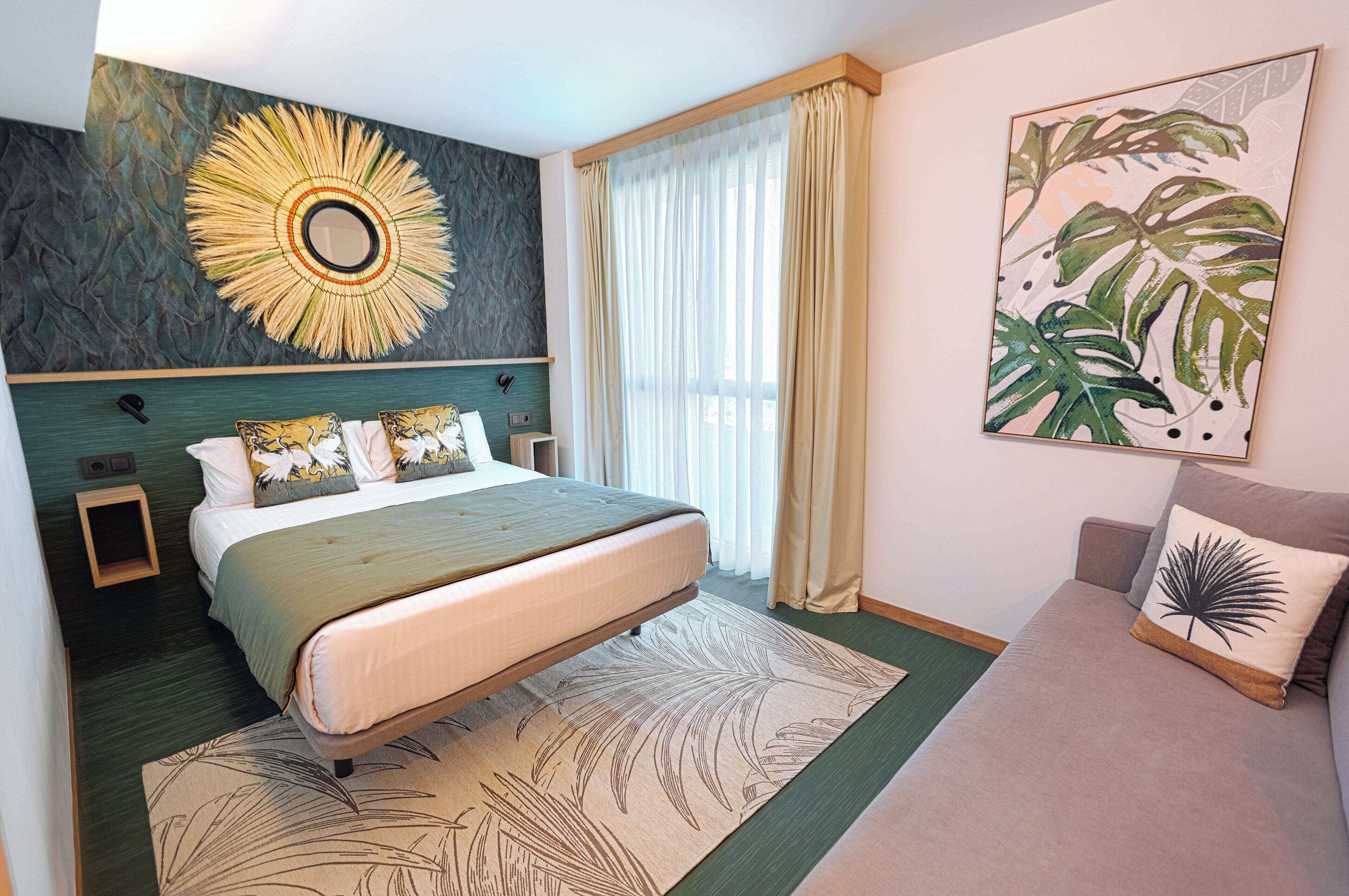 Habitación de hotel con una cama grande, un cabecero de diseño circular, una mesita de noche, un sofá y un ventanal con cortinas.