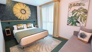 Habitación de hotel con una cama grande, un cabecero de diseño circular, una mesita de noche, un sofá y un ventanal con cortinas.