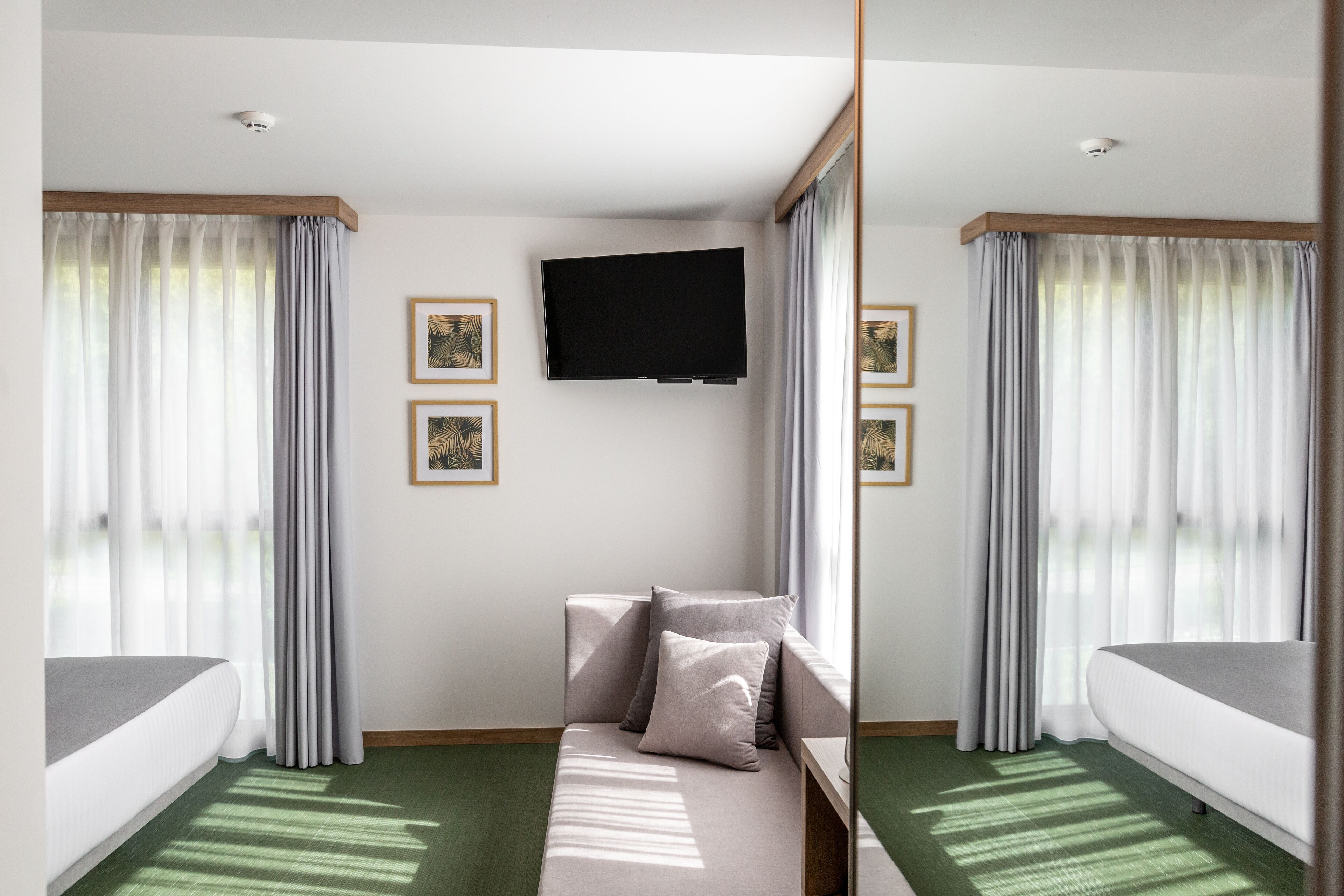 Une chambre d’hôtel avec un lit, un canapé, un téléviseur à écran plat fixé au mur et des rideaux aux fenêtres.