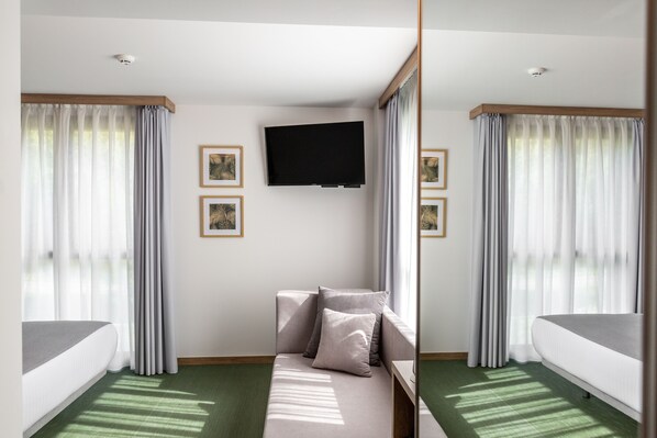 Habitación de hotel con cama, sofá, televisor de pantalla plana en la pared y cortinas en las ventanas.