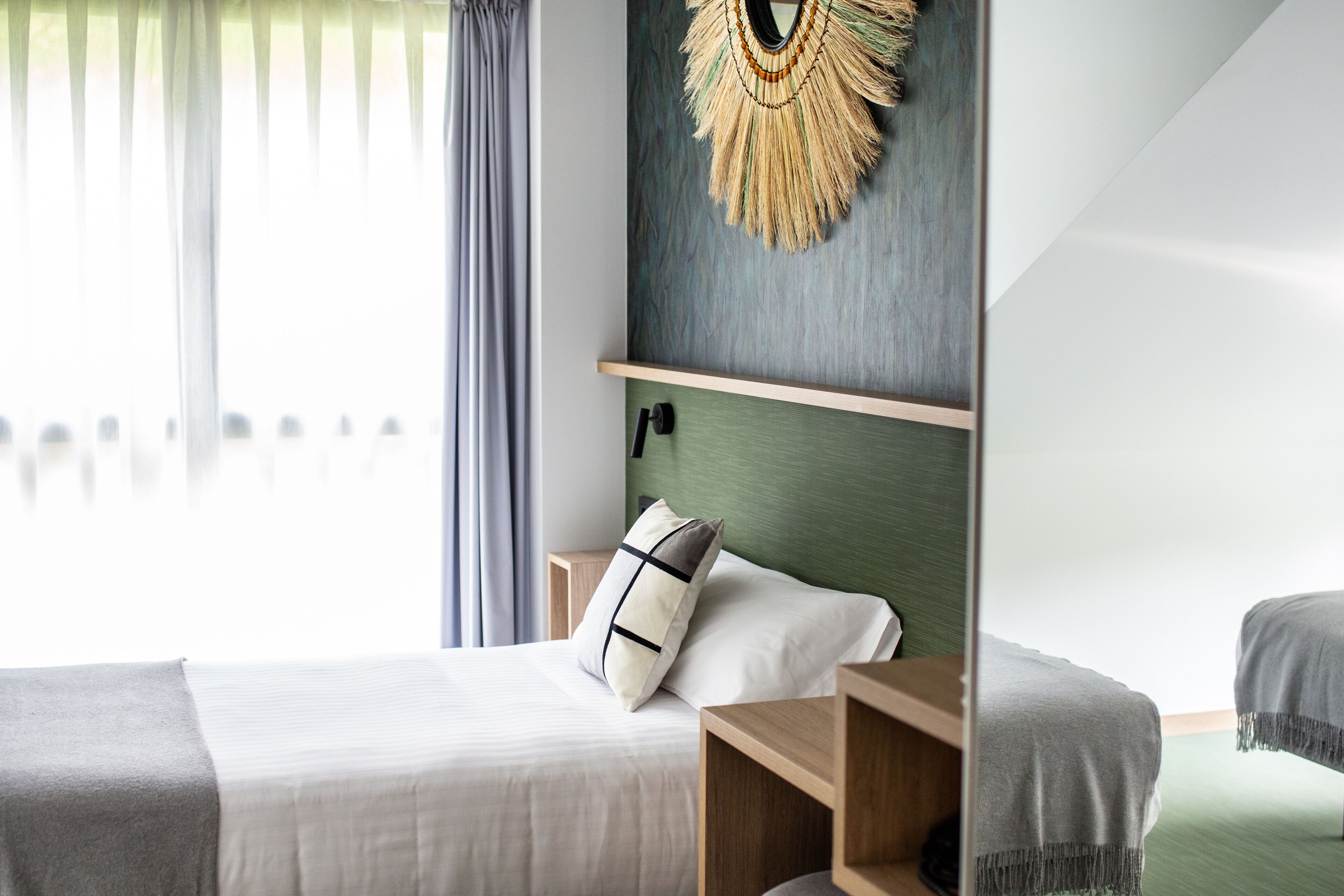 Een moderne hotelkamer met een bed, een houten nachtkastje, een decoratief wandobject en uitzicht op een balkon.