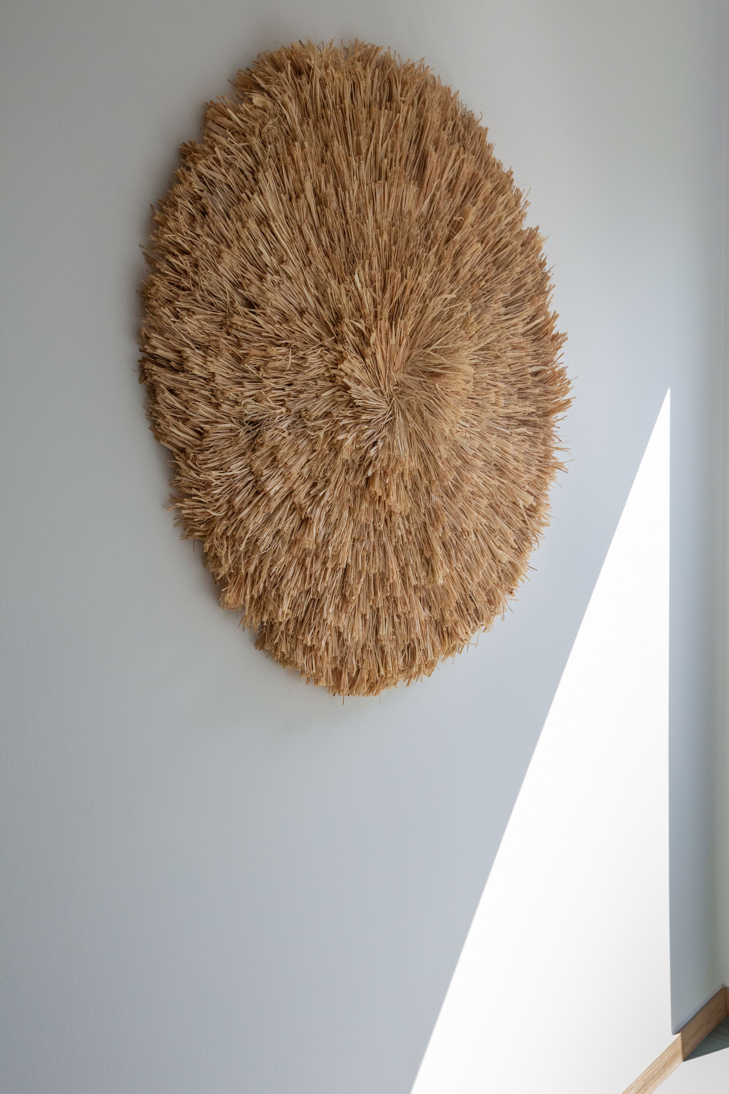 A circular woven wall hanging on a plain wall.