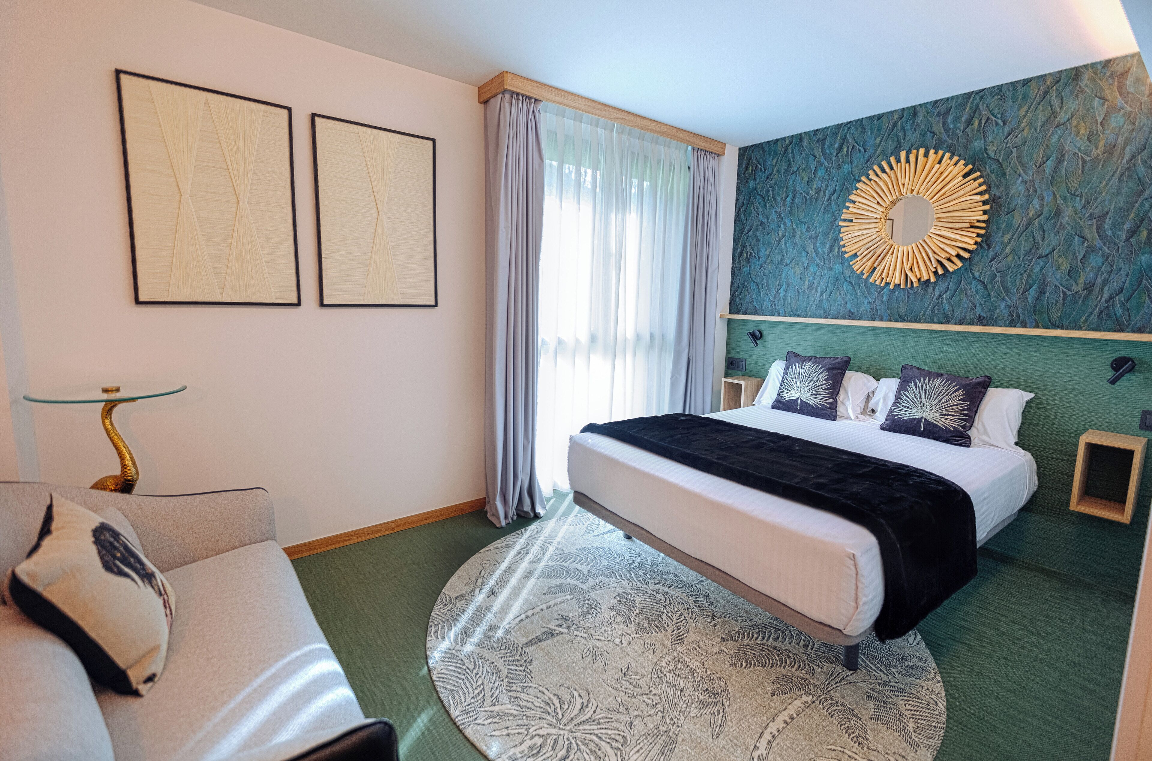 A hotel room with a bed, a sofa, a round rug, and two framed artworks on the wall.