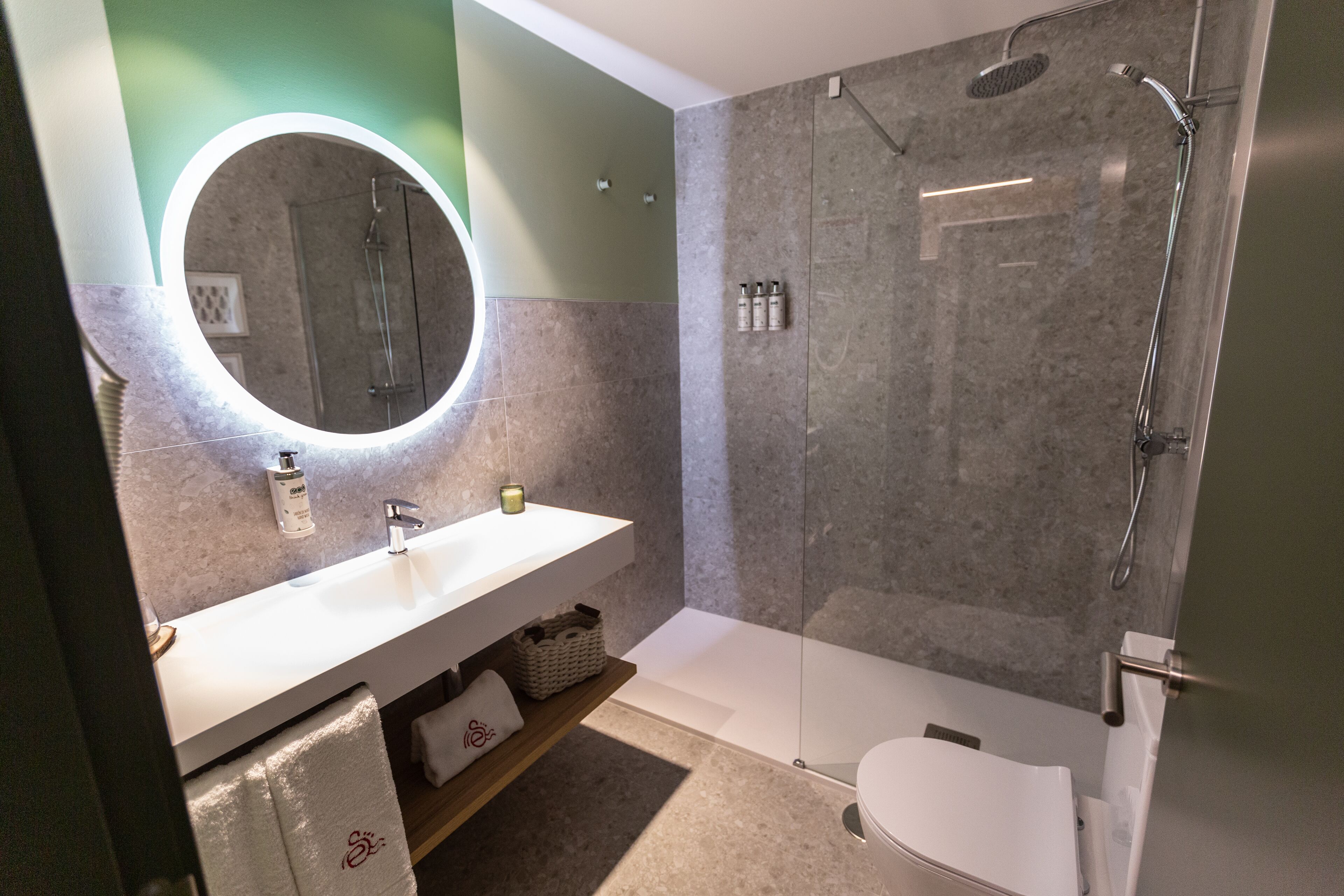 A modern bathroom with a white sink, a round mirror, and a glass-enclosed shower.