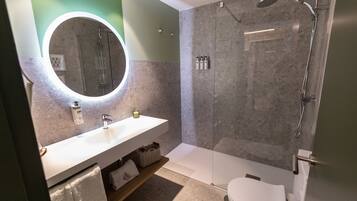 A modern bathroom with a white sink, a round mirror, and a glass-enclosed shower.