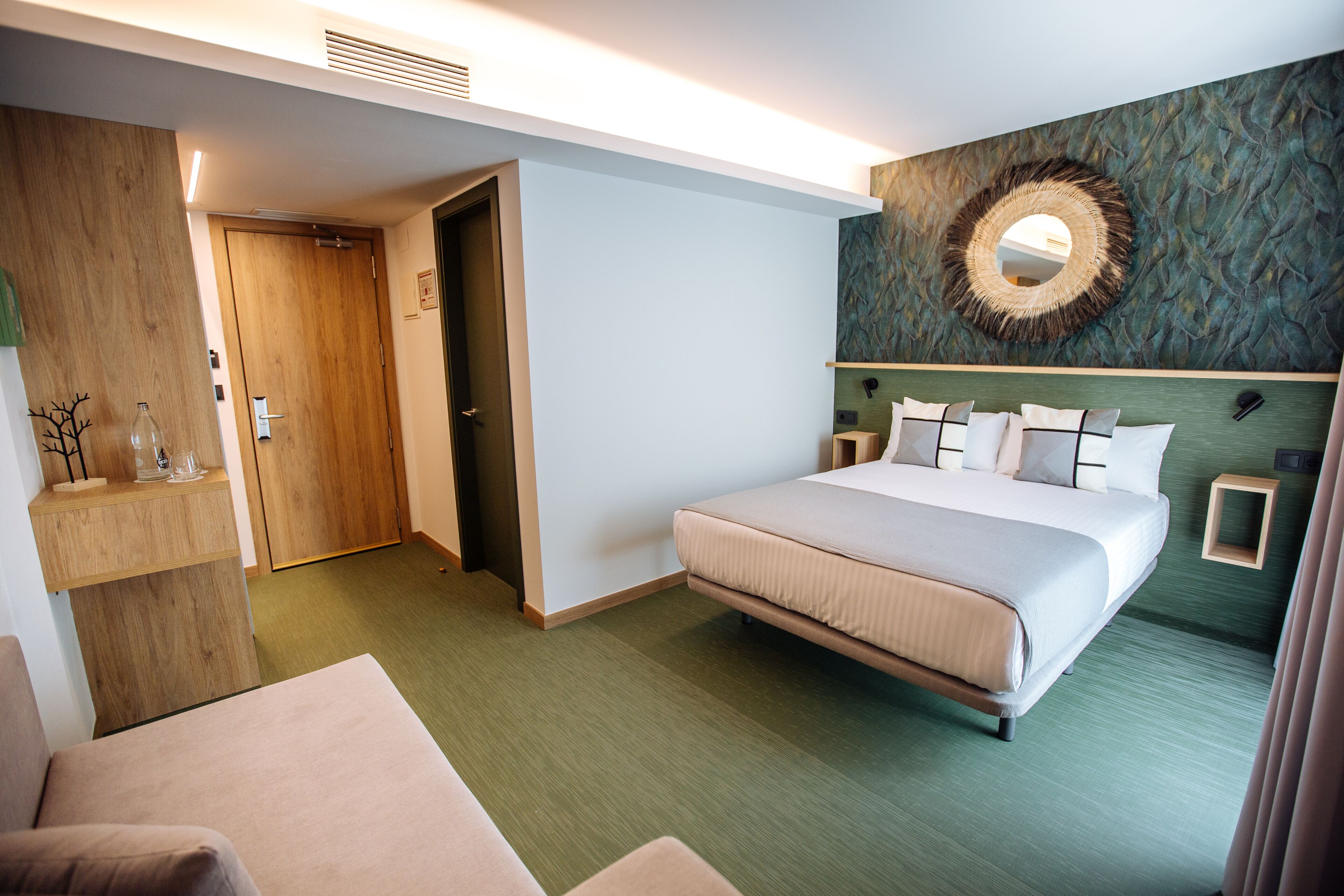 Une chambre d’hôtel avec un grand lit, une porte en bois, un miroir au mur et une moquette verte.