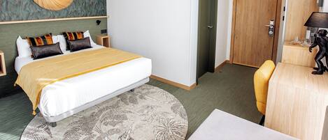 A hotel room with a bed, a round mirror, a wooden door, a desk, and a chair.