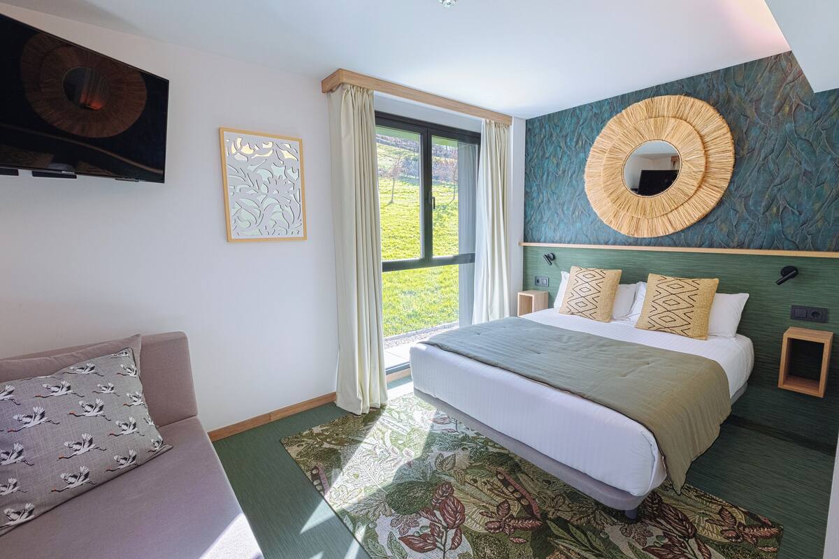 Quarto com cama, sofá, televisão e janela com cortinas.