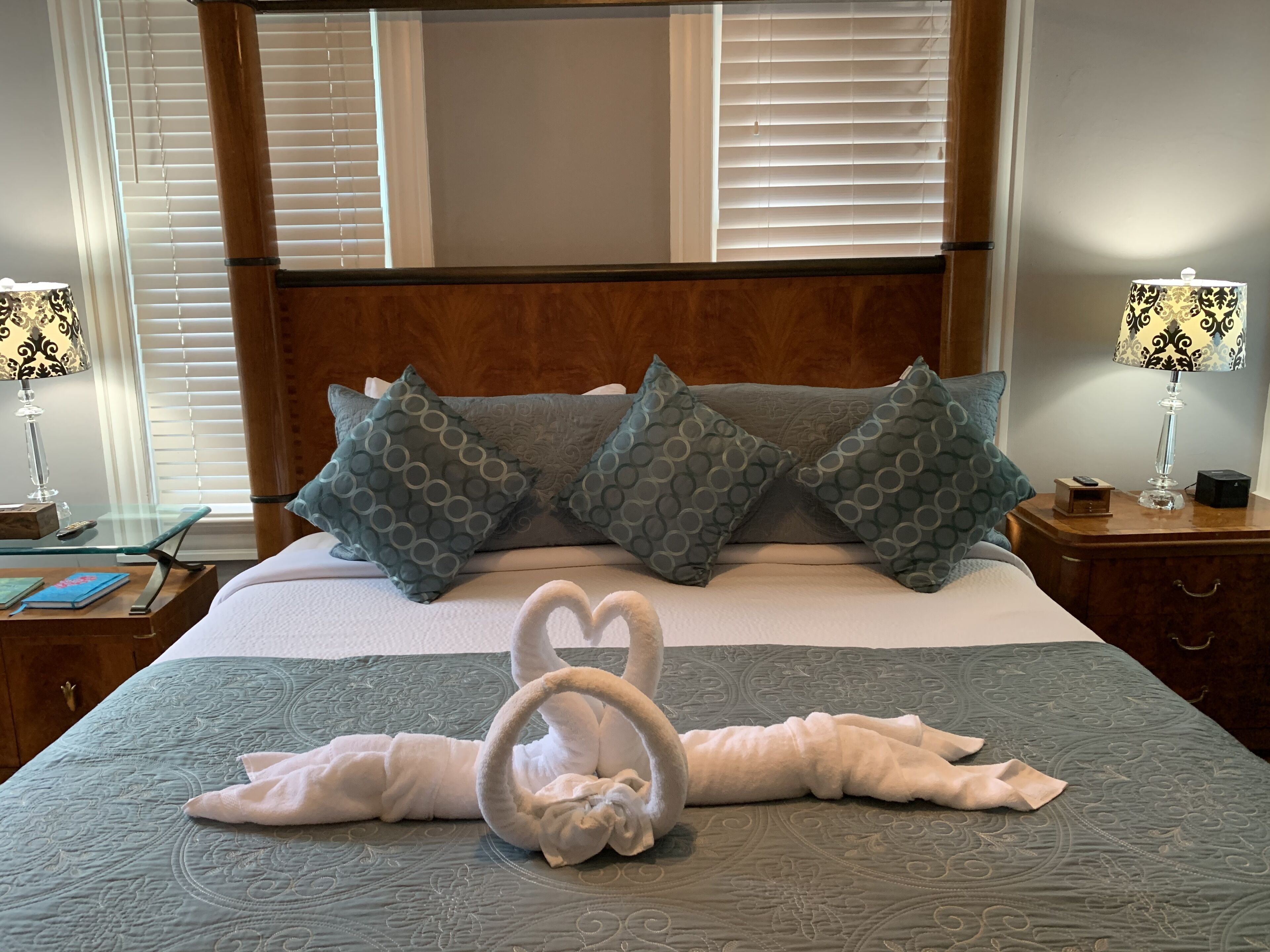 Una cama bien hecha con una escultura de toalla, cabecera de madera y almohadas estampadas.