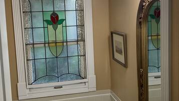 A bathroom with a bathtub, a sink, a large mirror, a chandelier, and a stained glass window.