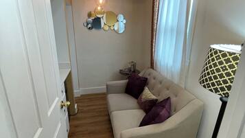 Een kamer met een beige bank, een witte deur, een plafondlamp en een lamp met een patroon.