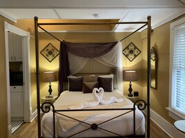 Una cama con dosel y cuatro columnas, dos lámparas de noche, espejos decorativos en la pared y una presentación de toallas con forma de cisne.