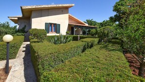 A modern house with a flat roof, a covered porch, and a well-maintained garden with various plants and a pathway leading to the entrance. - 3 bedroom pet friendly home in Marina di Modica (Marina di Modica)