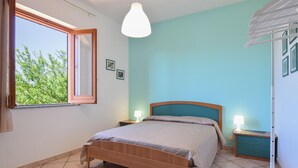 A bedroom with a wooden bed, two bedside tables with lamps, a window with a view of trees, and a teal-colored wall. - 3 bedroom pet friendly home in Marina di Modica (Marina di Modica)