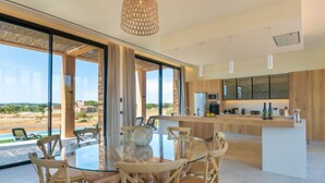 A modern kitchen with a central island, large windows, and a dining area with wicker chairs. - Can Navarro by Interhome (Inca)