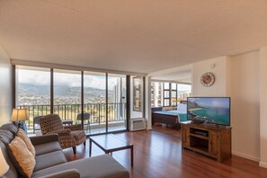Un salón amplio con un televisor grande, asientos cómodos y un balcón con vistas a la ciudad.