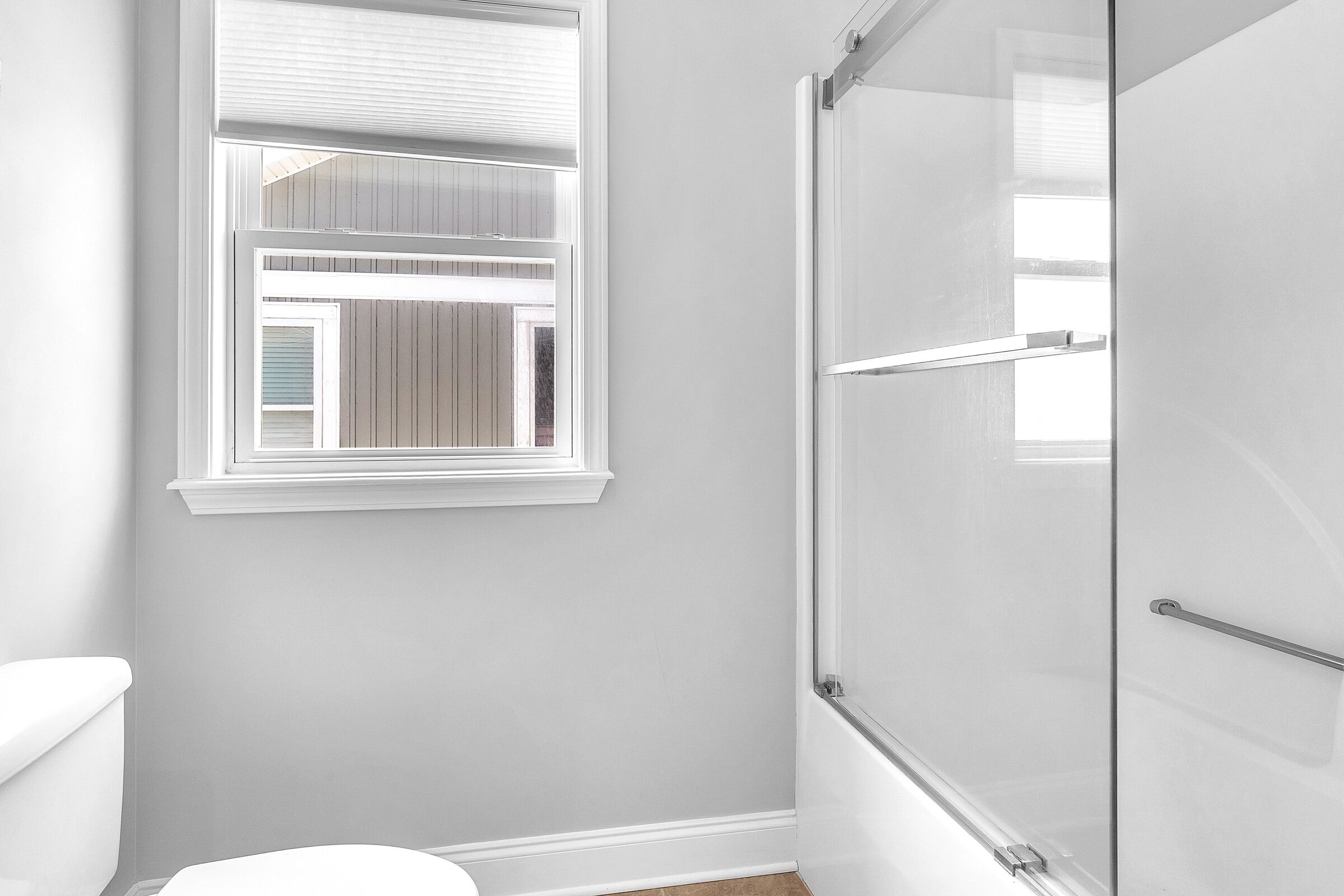 A bathroom with a toilet, a shower with a glass door, and a window with blinds.