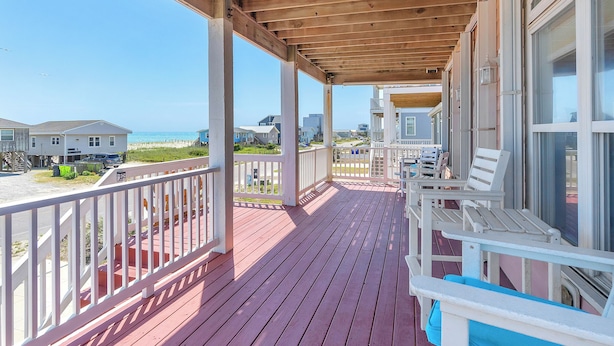 Een houten terras met een hek, met uitzicht op een strand en andere huizen.
