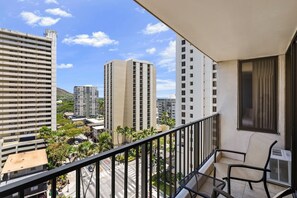 Ein Balkon mit Stuhl und Klimaanlage, der auf einen Stadtblick mit hohen Gebäuden und Palmen blickt.