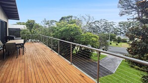 Une terrasse en bois avec une rambarde en métal, une table avec des chaises et une vue sur une rue et des espaces verts.