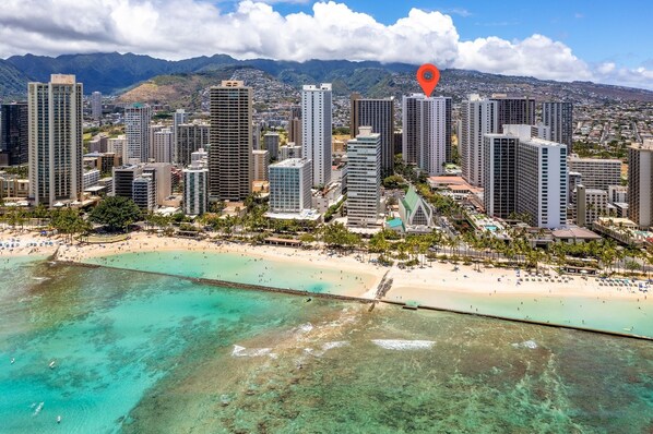A coastal cityscape with high-rise buildings, a beach, and a clear view of the mountains in the background.
