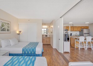 A hotel room with two beds, a kitchenette, and a dining area with chairs.
