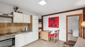 Una cucina compatta con mobili bianchi, forno integrato e zona pranzo con una sedia rossa e un tavolo.