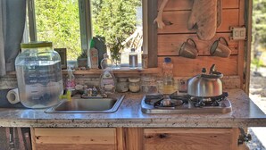 A rustic kitchen with a large water dispenser, a kettle, and various jars on the counter. - Rustic Moose Cabin Getaway - Glamping (Cantwell)