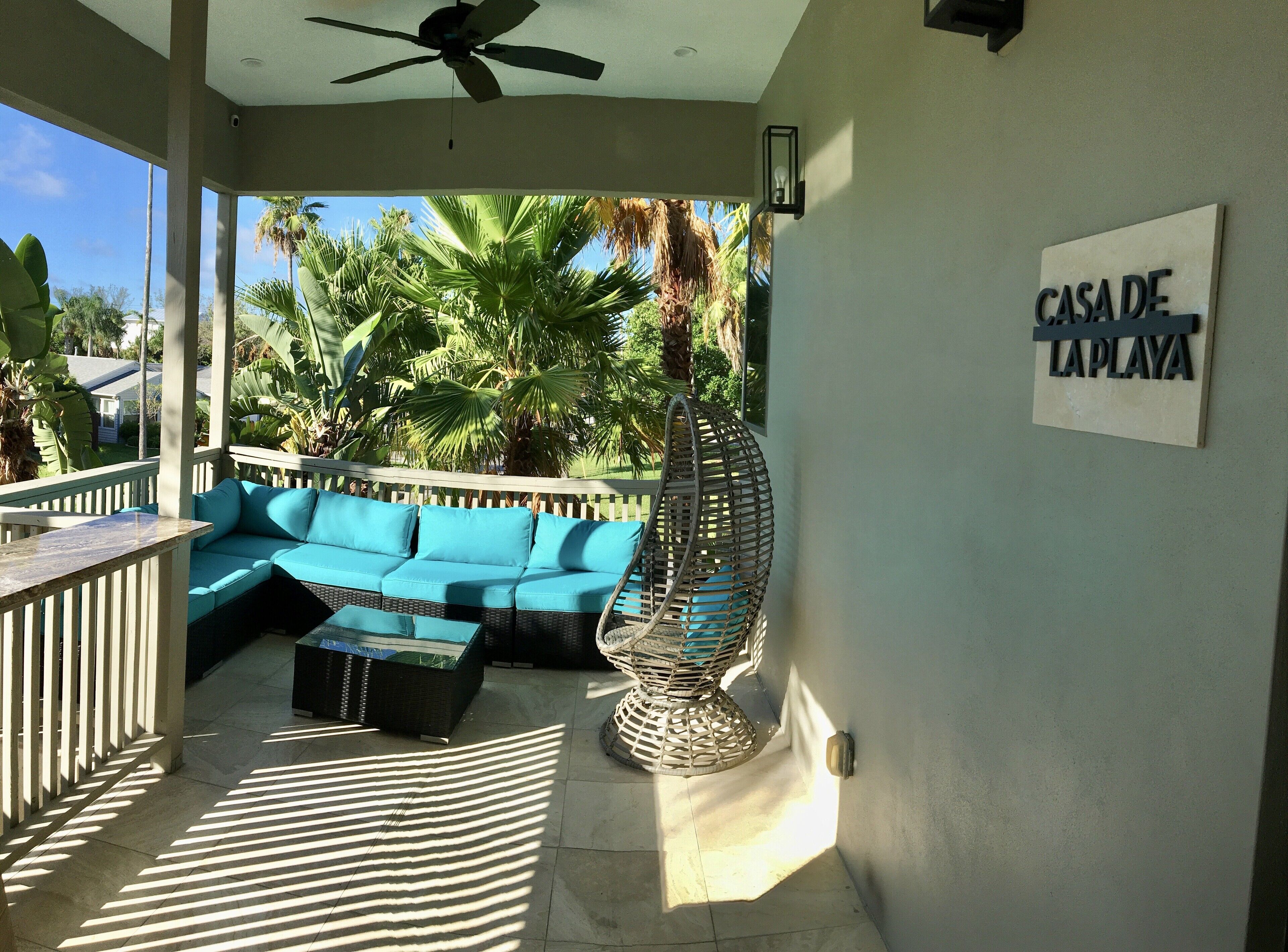 A covered outdoor seating area with a blue sofa, a wicker chair, and a striped rug.