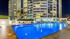 Un hôtel moderne doté d’une grande piscine extérieure, de nombreux balcons et d’une façade bien éclairée.