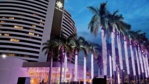 Un hôtel moderne à la façade incurvée, agrémenté de palmiers et de structures verticales illuminées.