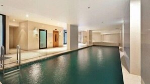 Une piscine dotée d’une terrasse carrelée, d’une porte en bois et d’un mur en verre.