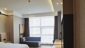 A modern hotel room with a large bed, a seating area with a bench, a flat-screen TV, and a large window with curtains.