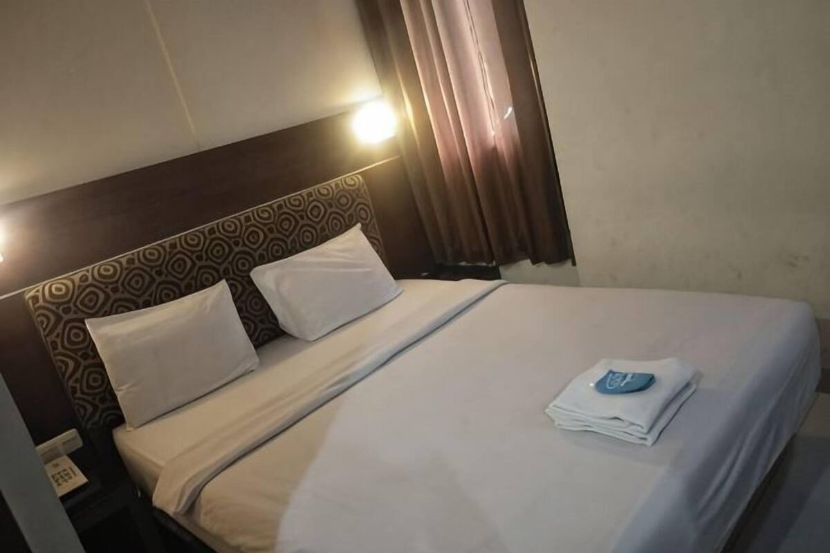 A hotel room with a bed, a headboard with a patterned design, a bedside table with a phone, and a window with curtains.