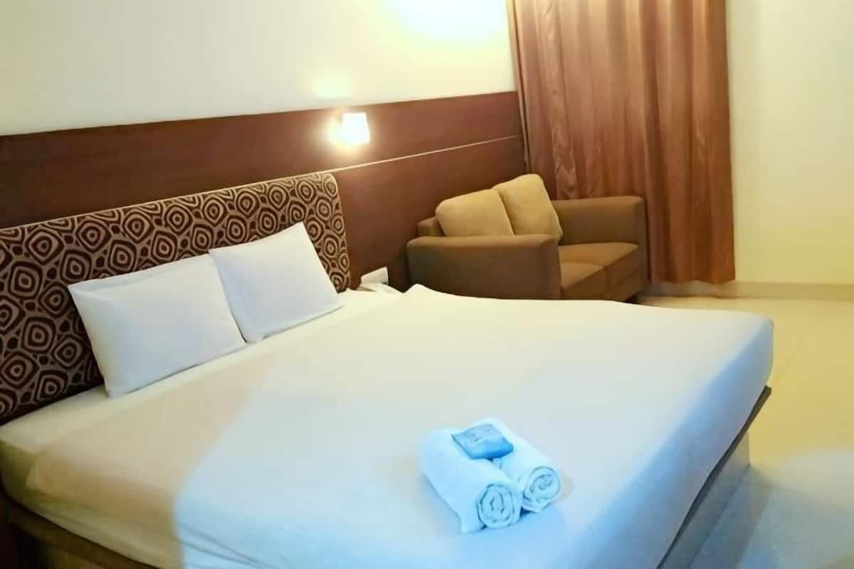 A hotel room with a large bed, a headboard with a geometric pattern, a small armchair, and a curtain.