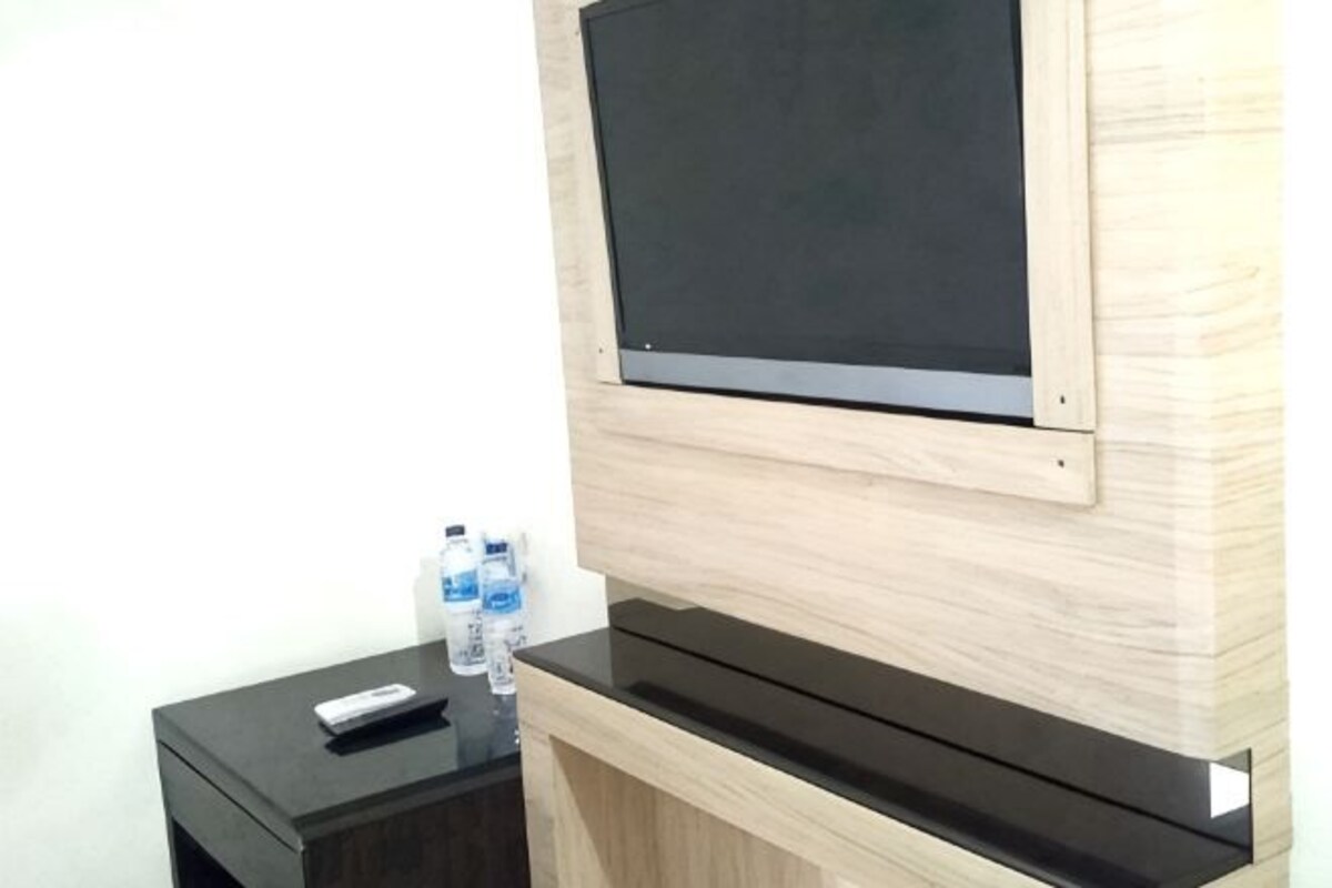 Habitación con televisión de pantalla plana montada en la pared, una encimera negra y una pequeña mesita de madera con un control remoto y botellas de agua.