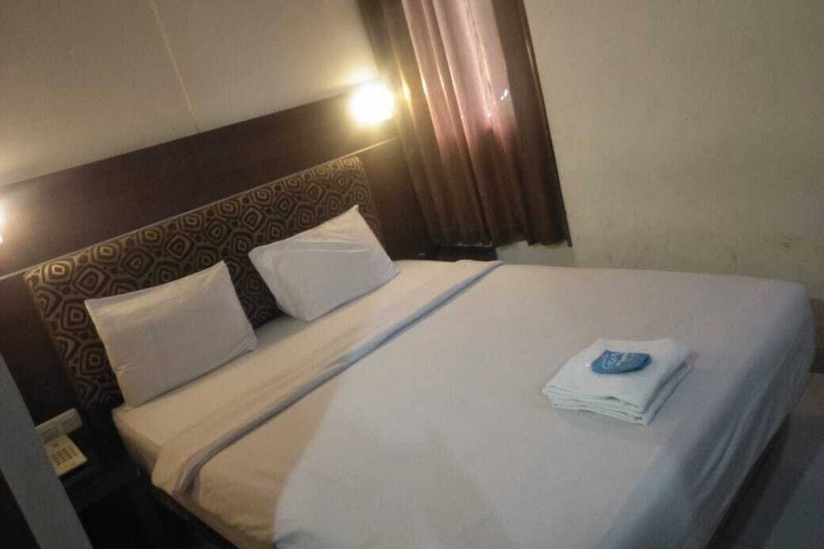 A hotel room with a neatly made bed, a headboard with a patterned design, and a bedside table with a lamp.