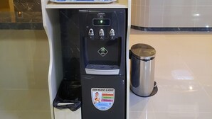 A hotel reception area with a water dispenser, a trash bin, and a sign offering free Wi-Fi to guests. - Ams Penthouse (Jakarta)