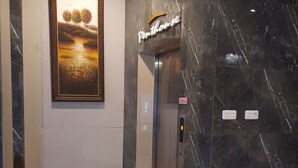 A modern elevator with a marble wall and a framed painting of trees. - Ams Penthouse (Jakarta)