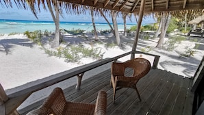 A wooden deck with wicker chairs overlooking a beach with a hammock and palm trees. - Aotera Guest House (Rangiroa)