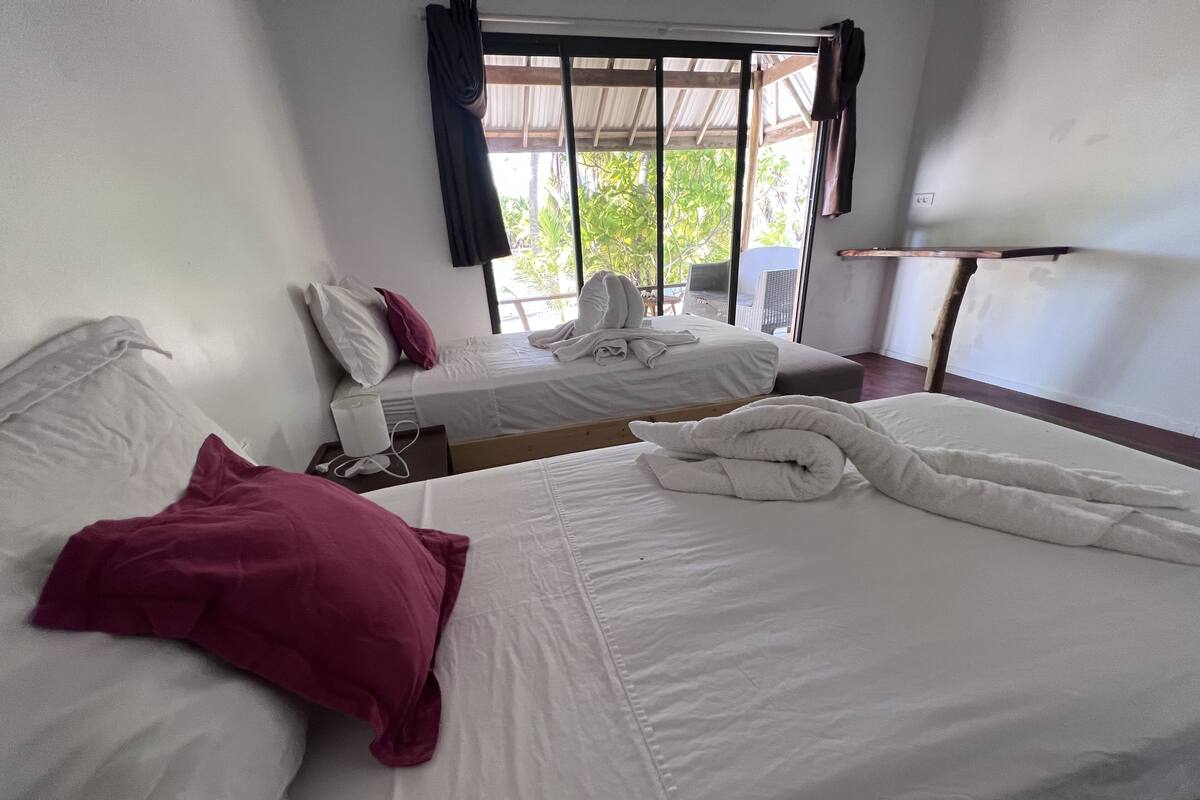 A hotel room with two beds, a window with curtains, and a small table.