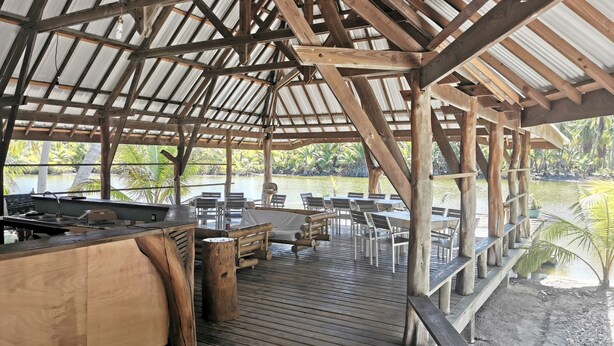 Een houten terras met tafels en stoelen, een barbecue en uitzicht op een meer.