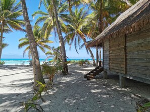 Eine Strandhütte mit einem Reetdach, umgeben von Palmen und einem Sandstrand.