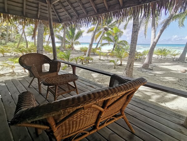 A wooden deck with wicker furniture overlooking a beach with palm trees and the ocean.