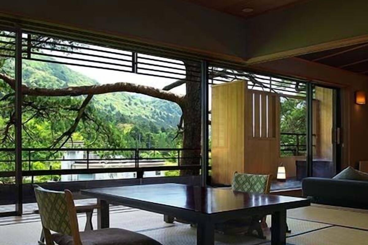 Une pièce de style japonais traditionnel, avec un sol recouvert de tatamis, une table basse et une vue sur une végétation luxuriante.