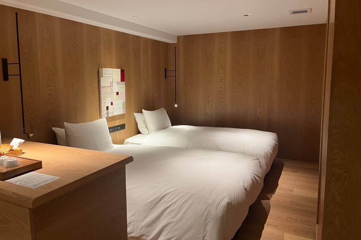 Une chambre d’hôtel avec un mur lambrissé en bois, un lit avec une literie blanche, un bureau avec une lampe et un tableau d’affichage.