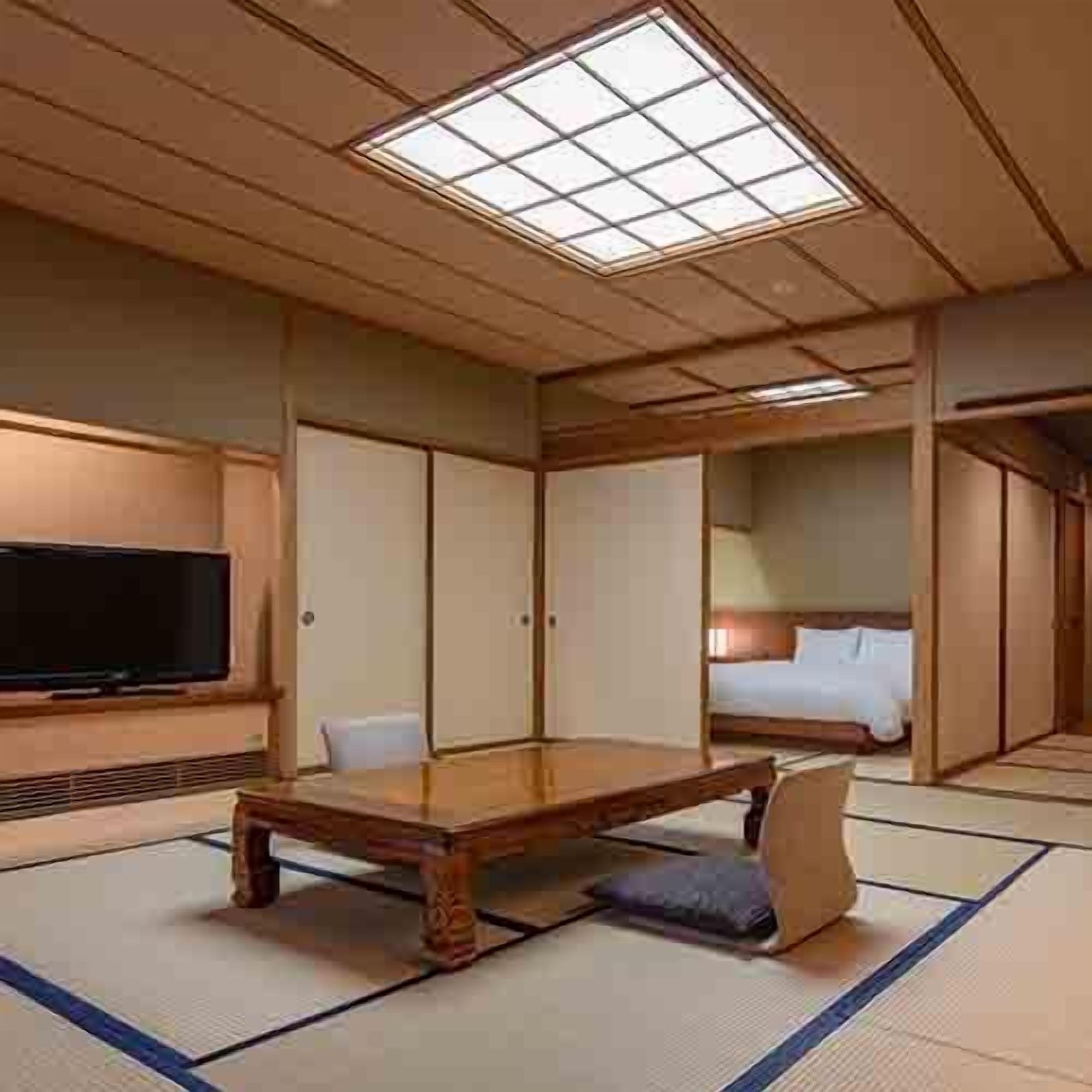 A traditional Japanese-style room with tatami flooring, a low wooden table, a bed with a white mattress, and a television on the wall.