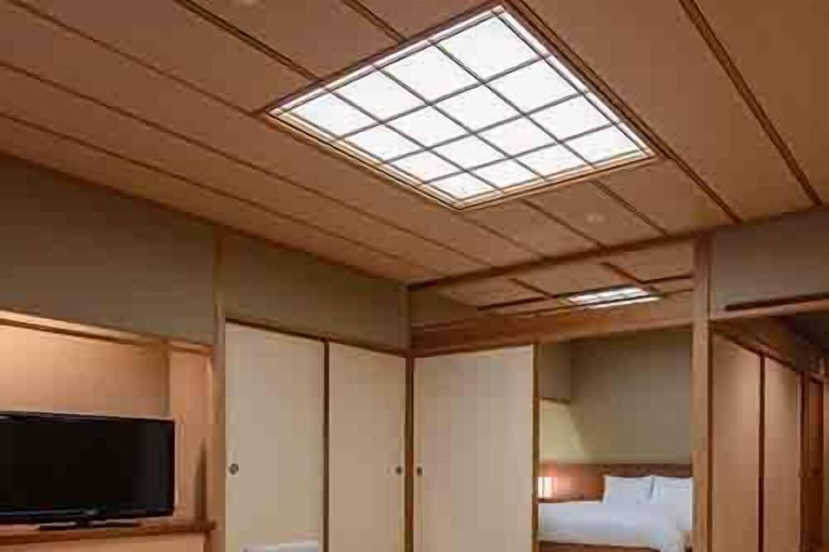 Une pièce de style japonais traditionnel, avec un sol recouvert de tatamis, une petite table en bois, un lit doté d’un matelas blanc et un téléviseur fixé au mur.